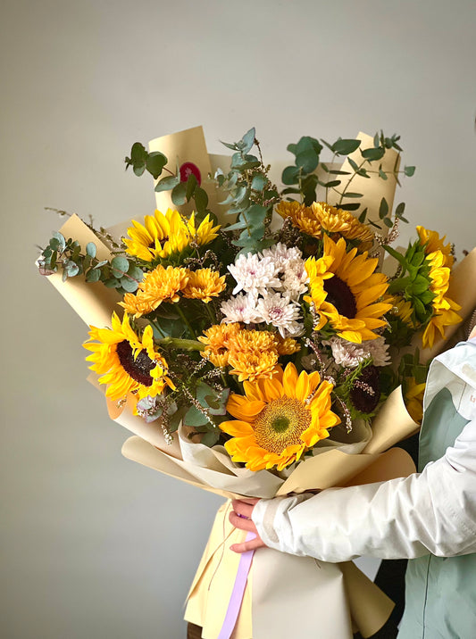 A bouquet of Sunflowers, mix of carnations and foliages wrapped in a brown paper bouquet by Five Petals Florist.