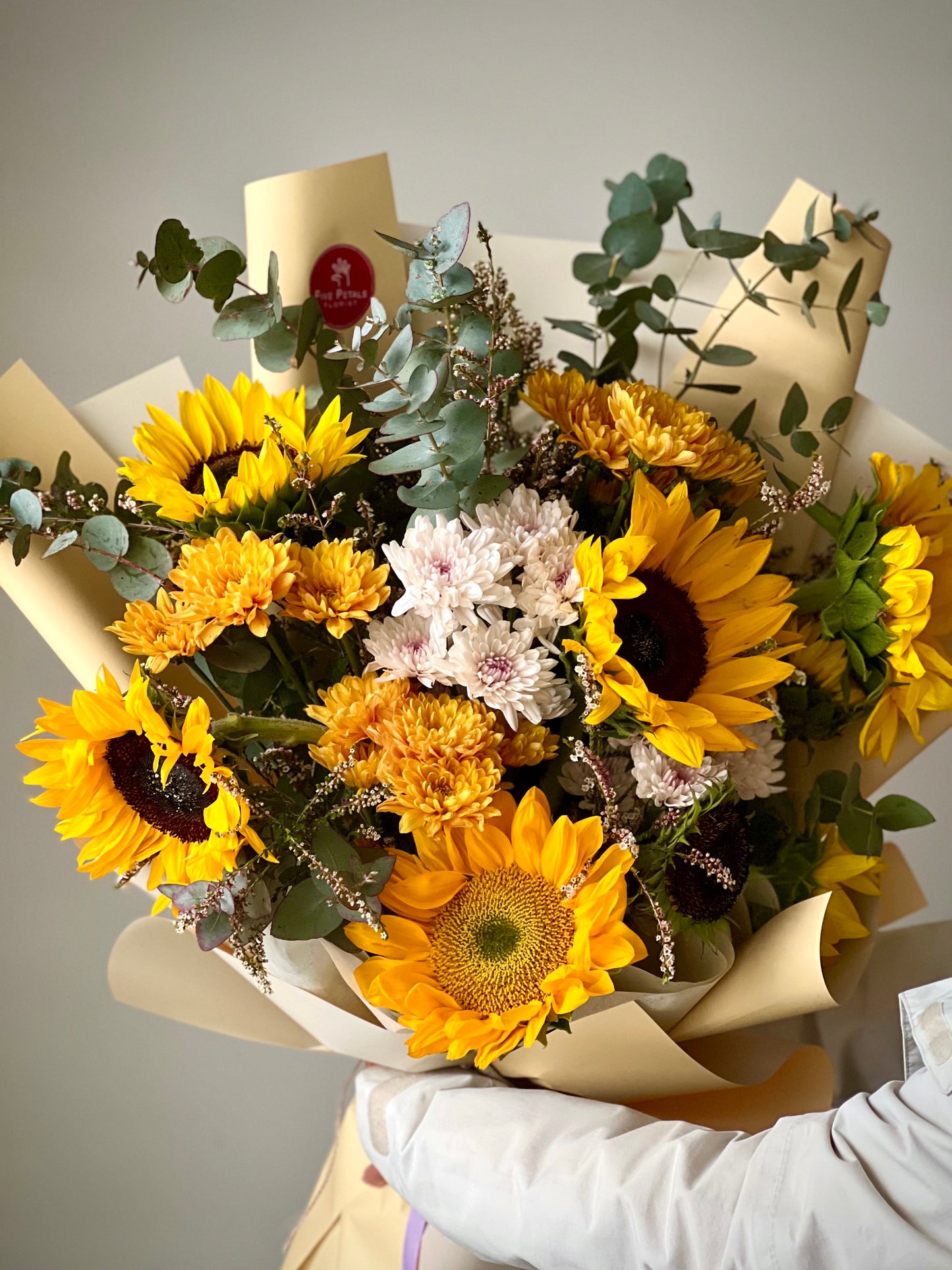 A bouquet of Sunflowers, mix of carnations and foliages wrapped in a brown paper bouquet by Five Petals Florist.