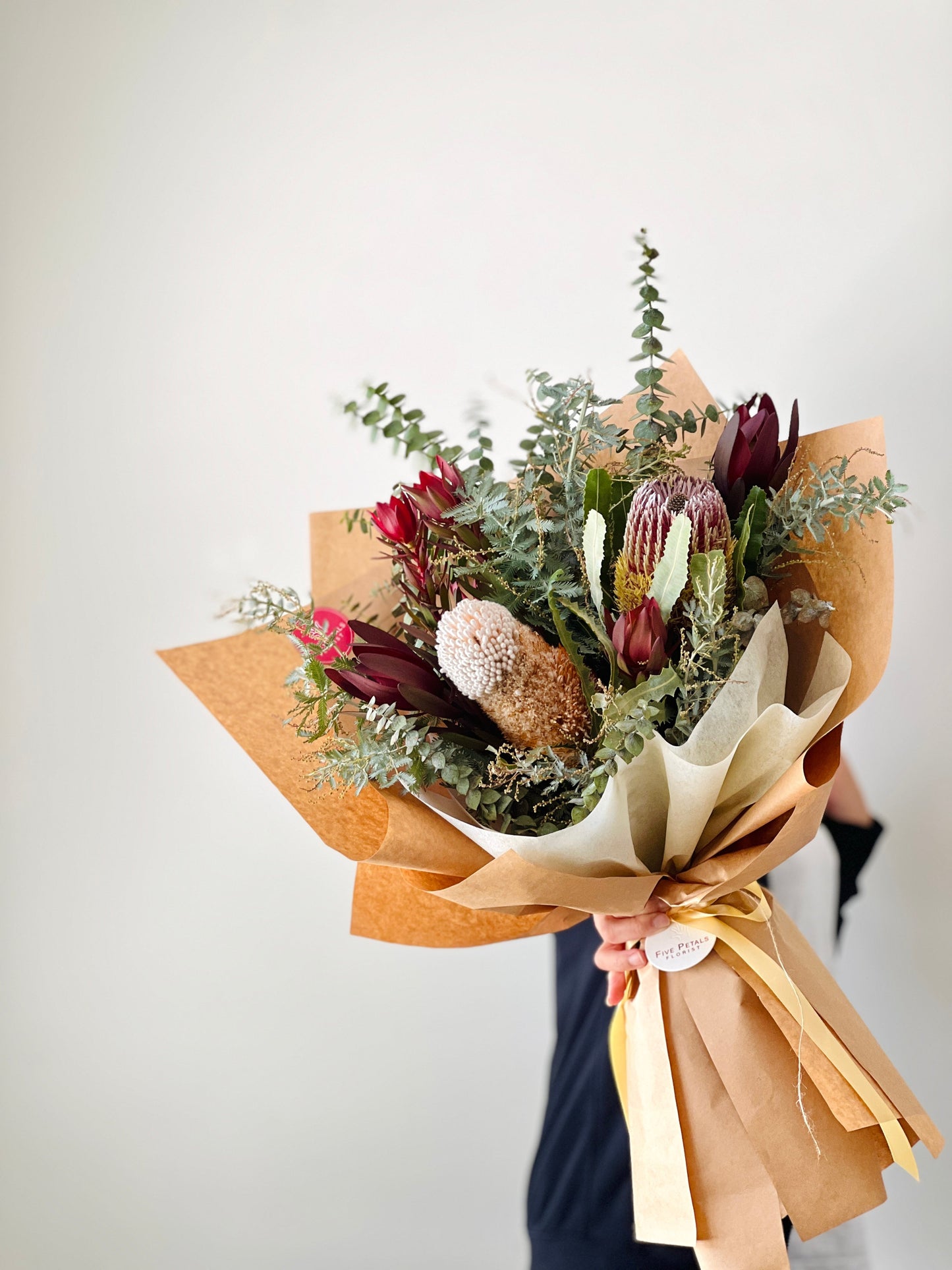 Native flowers and foliages in a bouquet wrapped in brown paper.