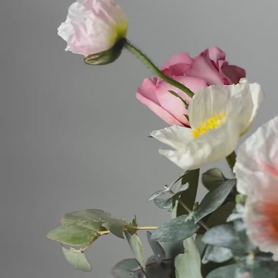 Vibrant flower arrangement in a pastel green box with pink ribbon, featuring poppies, roses, eucalyptus, and delicate blooms from Five Petals Florist.