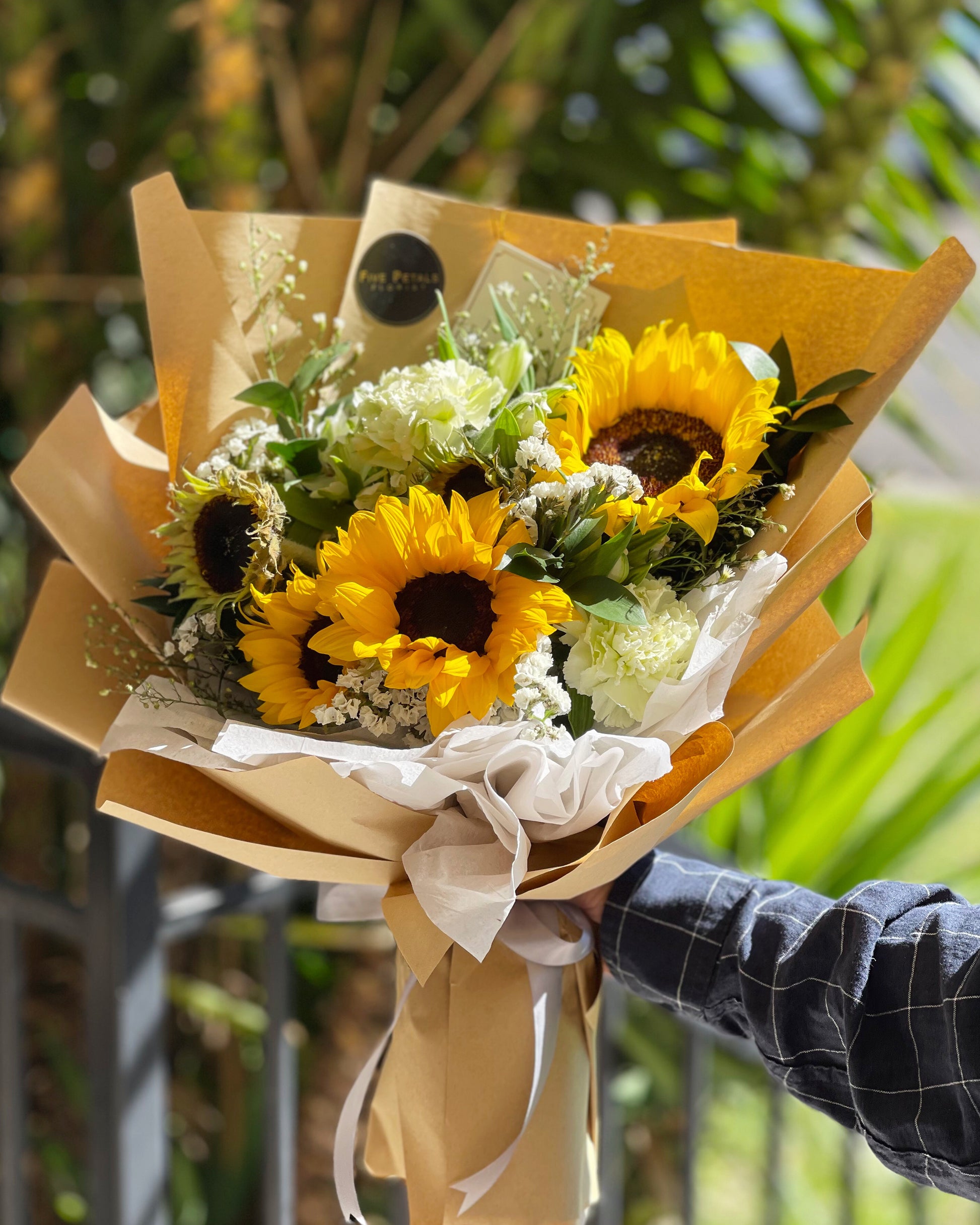 A bouquet of Sunflowers, mix of carnations and foliages wrapped in a brown paper bouquet by Five Petals Florist.